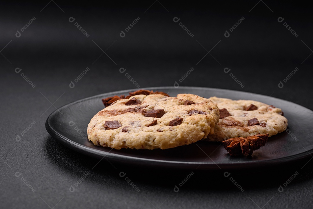 Deliciosos biscoitos de aveia crocantes e frescos com chocolate e nozes em uma placa de cerâmica preta sobre um fundo escuro de concreto