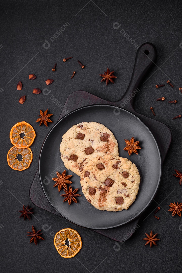 Deliciosos biscoitos de aveia crocantes e frescos com chocolate e nozes em uma placa de cerâmica preta sobre um fundo escuro de concreto