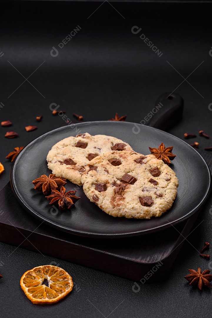 Deliciosos biscoitos de aveia crocantes e frescos com chocolate e nozes em uma placa de cerâmica preta sobre um fundo escuro de concreto