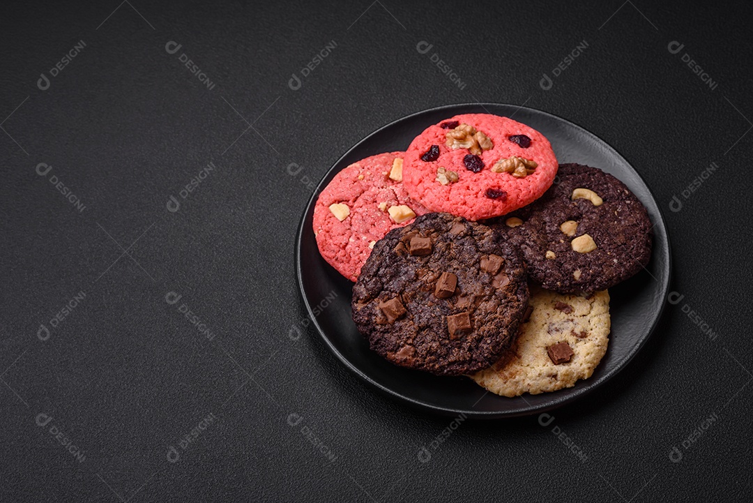 Deliciosos biscoitos de aveia crocantes e frescos com chocolate e nozes em uma placa de cerâmica preta sobre um fundo escuro de concreto