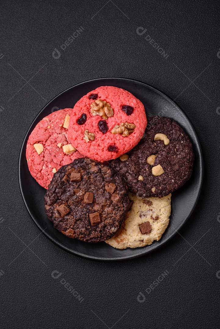 Deliciosos biscoitos de aveia crocantes e frescos com chocolate e nozes em uma placa de cerâmica preta sobre um fundo escuro de concreto
