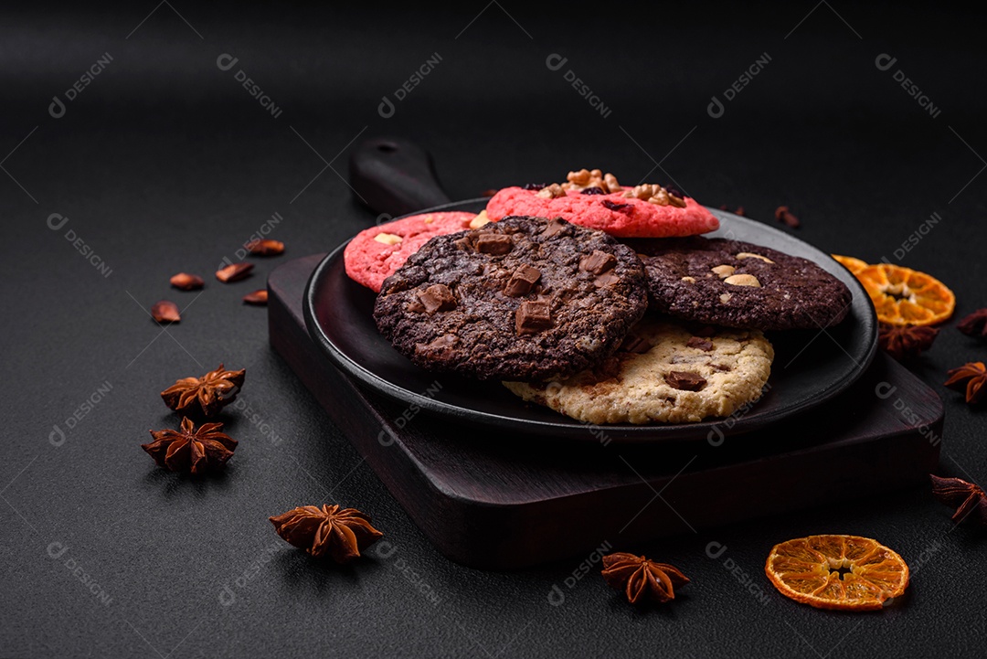 Deliciosos biscoitos de aveia crocantes e frescos com chocolate e nozes em uma placa de cerâmica preta sobre um fundo escuro de concreto