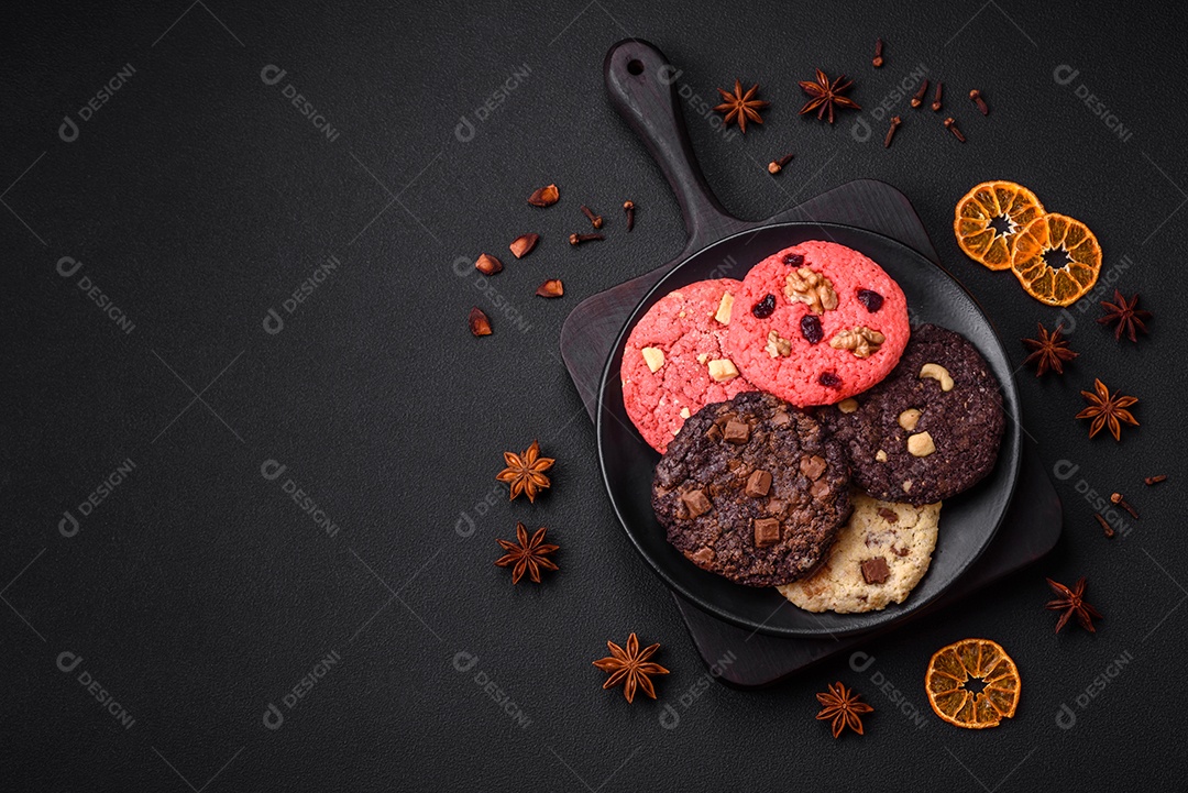 Deliciosos biscoitos de aveia crocantes e frescos com chocolate e nozes em uma placa de cerâmica preta sobre um fundo escuro de concreto