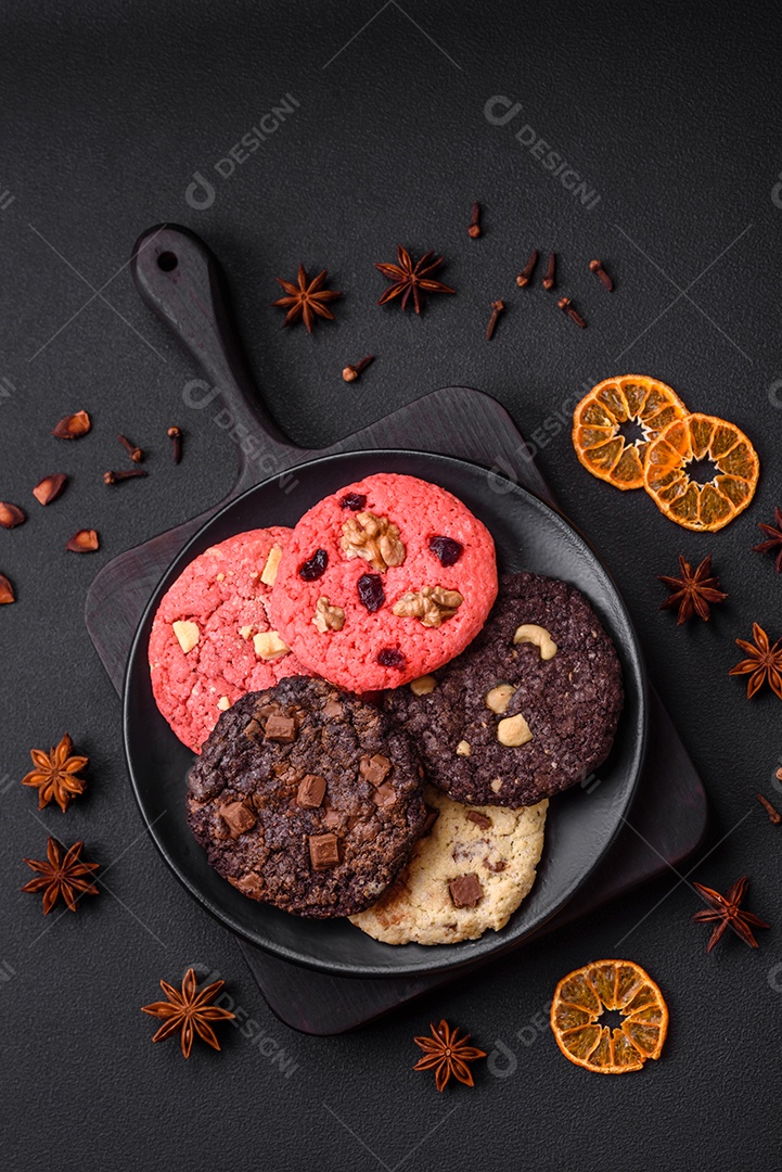 Deliciosos biscoitos de aveia crocantes e frescos com chocolate e nozes em uma placa de cerâmica preta sobre um fundo escuro de concreto