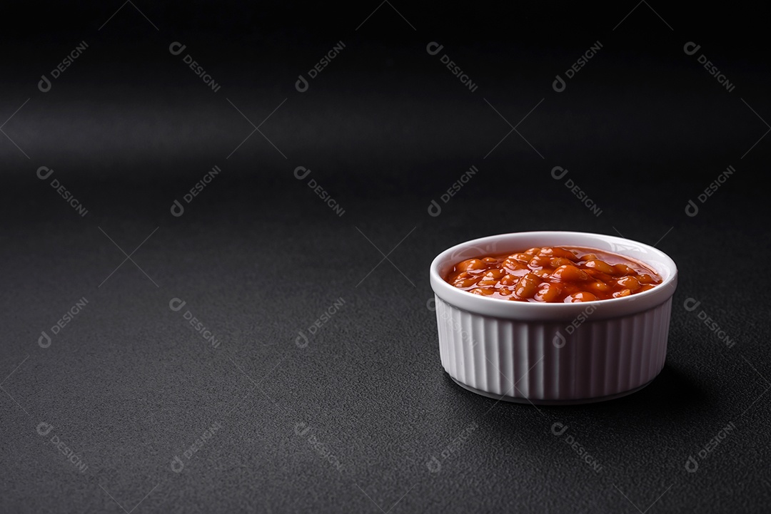 Deliciosos feijões enlatados em um tomate em uma tigela de cerâmica branca sobre um fundo escuro de concreto