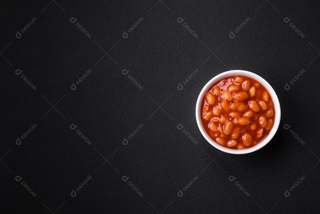 Deliciosos feijões enlatados em um tomate em uma tigela de cerâmica branca sobre um fundo escuro de concreto