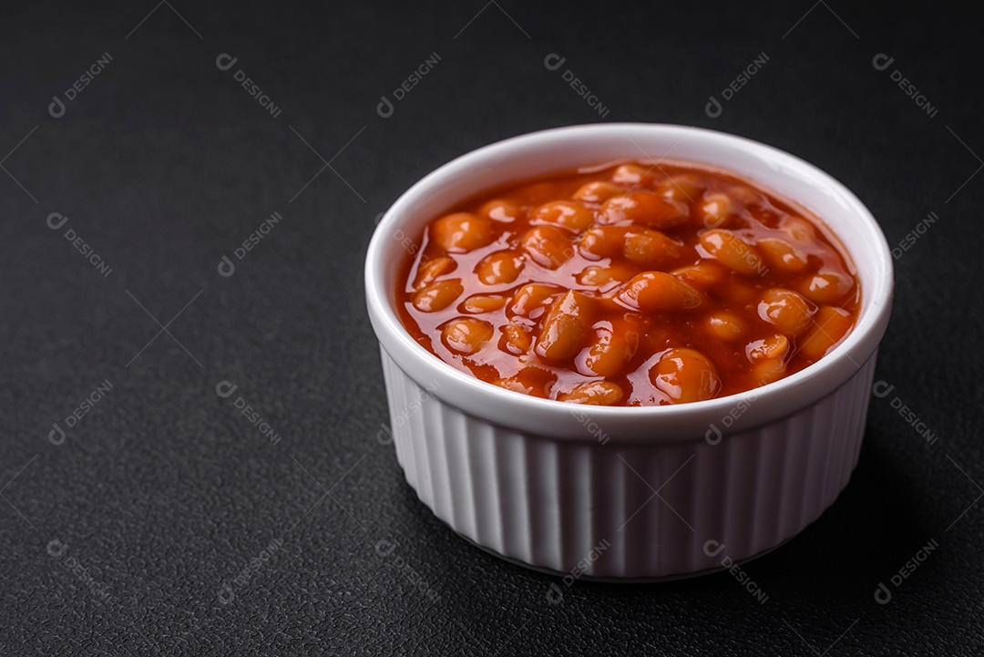 Deliciosos feijões enlatados em um tomate em uma tigela de cerâmica branca sobre um fundo escuro de concreto