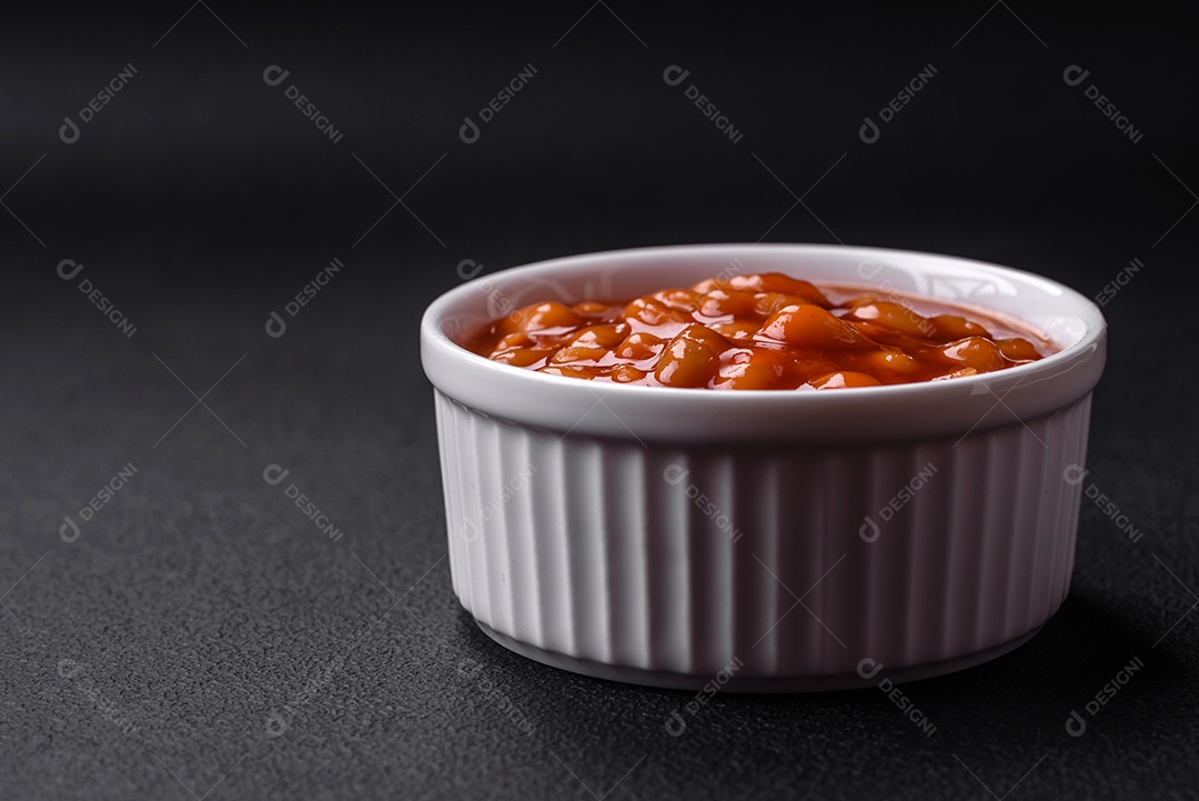 Deliciosos feijões enlatados em um tomate em uma tigela de cerâmica branca sobre um fundo escuro de concreto