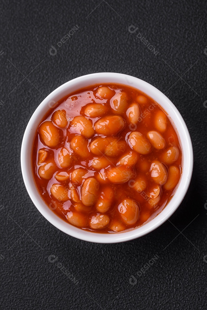 Deliciosos feijões enlatados em um tomate em uma tigela de cerâmica branca sobre um fundo escuro de concreto