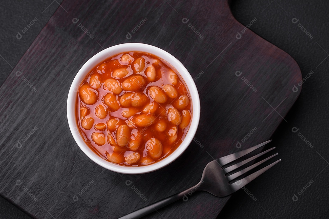 Deliciosos feijões enlatados em um tomate em uma tigela de cerâmica branca sobre um fundo escuro de concreto