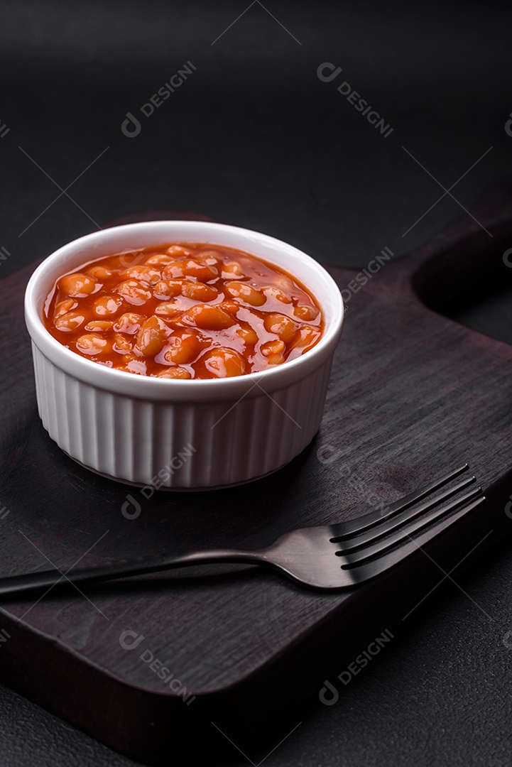 Deliciosos feijões enlatados em um tomate em uma tigela de cerâmica branca sobre um fundo escuro de concreto