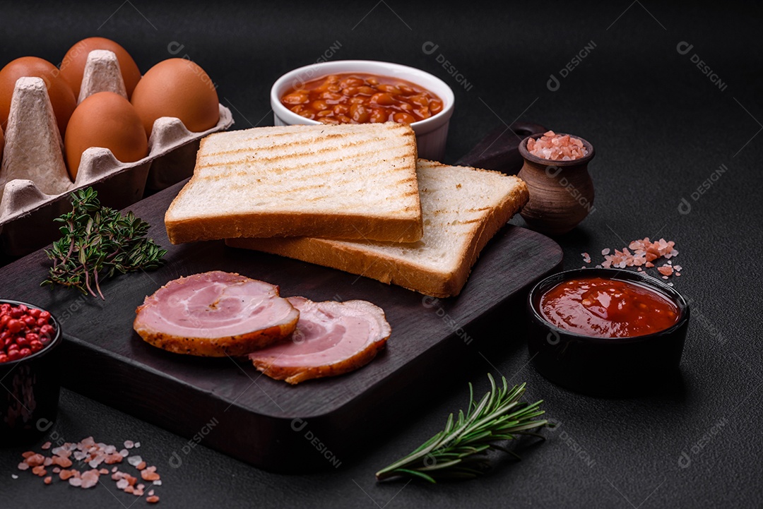 Delicioso café da manhã inglês nutritivo com ovos fritos, tomates, bacon e feijão em um fundo escuro de concreto