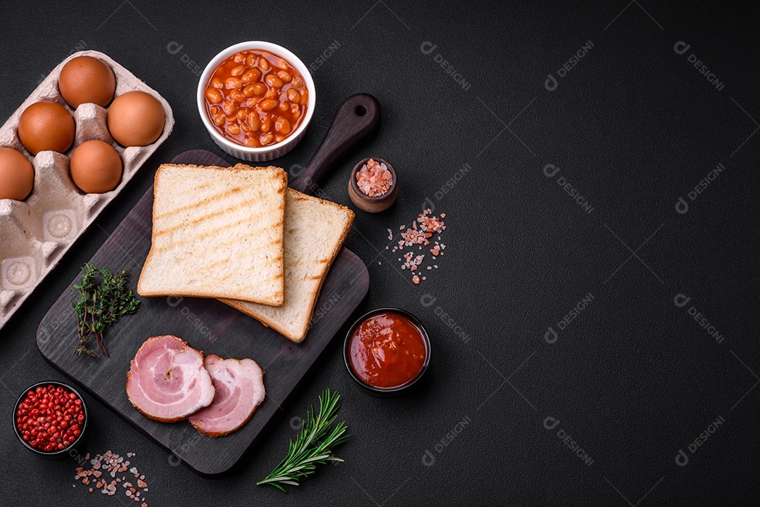Delicioso café da manhã inglês nutritivo com ovos fritos, tomates, bacon e feijão em um fundo escuro de concreto