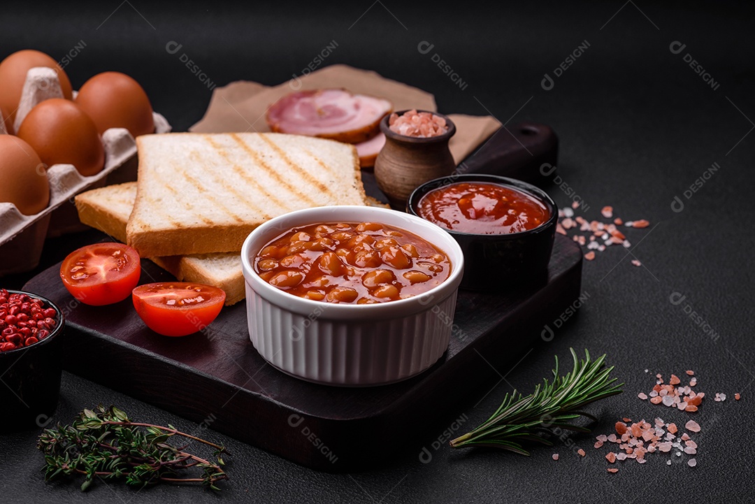 Deliciosos feijões enlatados em um tomate em uma tigela de cerâmica branca sobre um fundo escuro de concreto