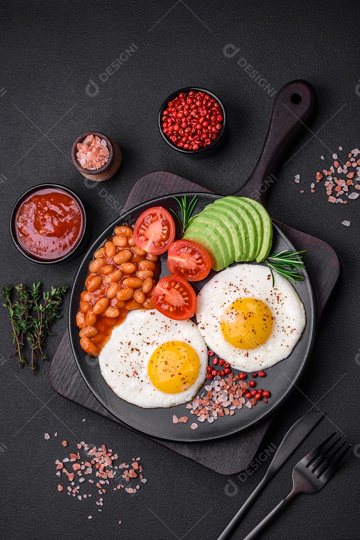 Delicioso café da manhã inglês nutritivo com ovos fritos, tomates, bacon e feijão em um fundo escuro de concreto
