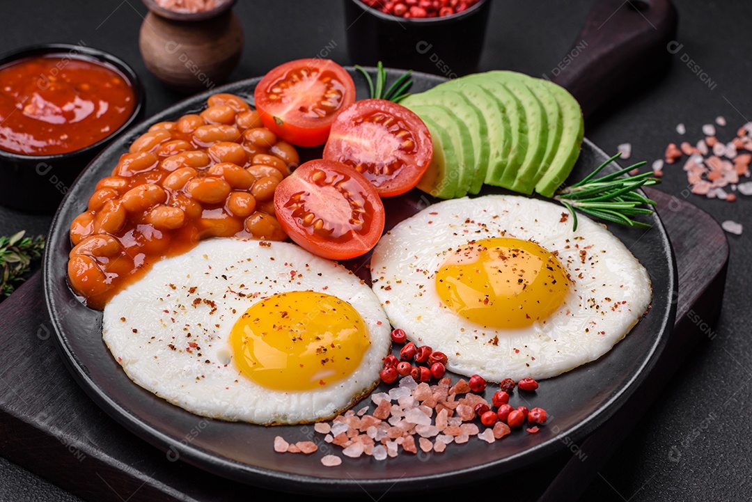 Delicioso café da manhã inglês nutritivo com ovos fritos, tomates, bacon e feijão em um fundo escuro de concreto