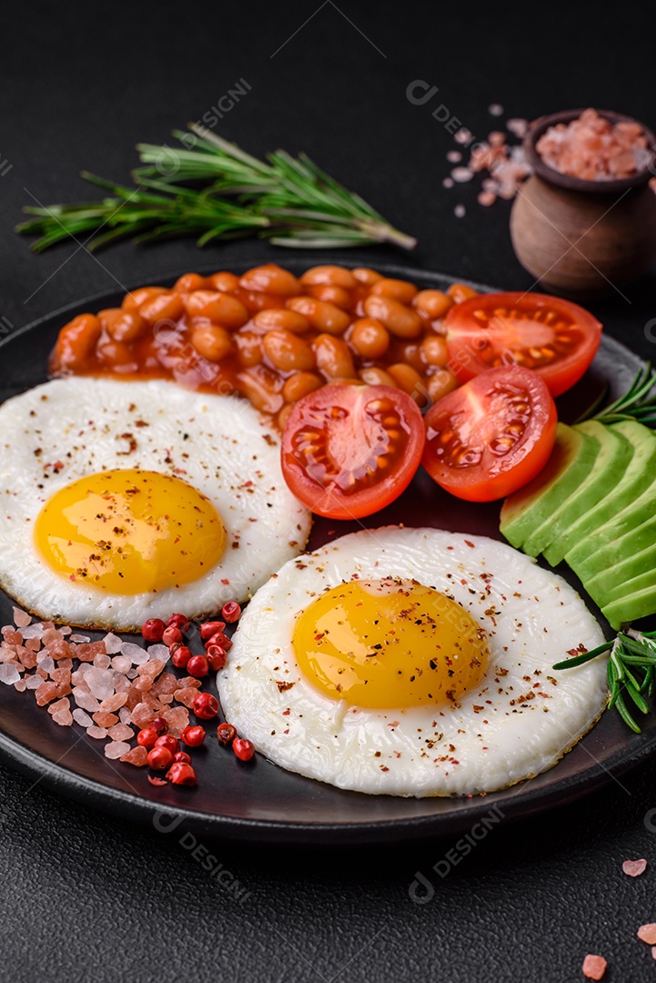 Delicioso café da manhã inglês nutritivo com ovos fritos, tomates, bacon e feijão em um fundo escuro de concreto