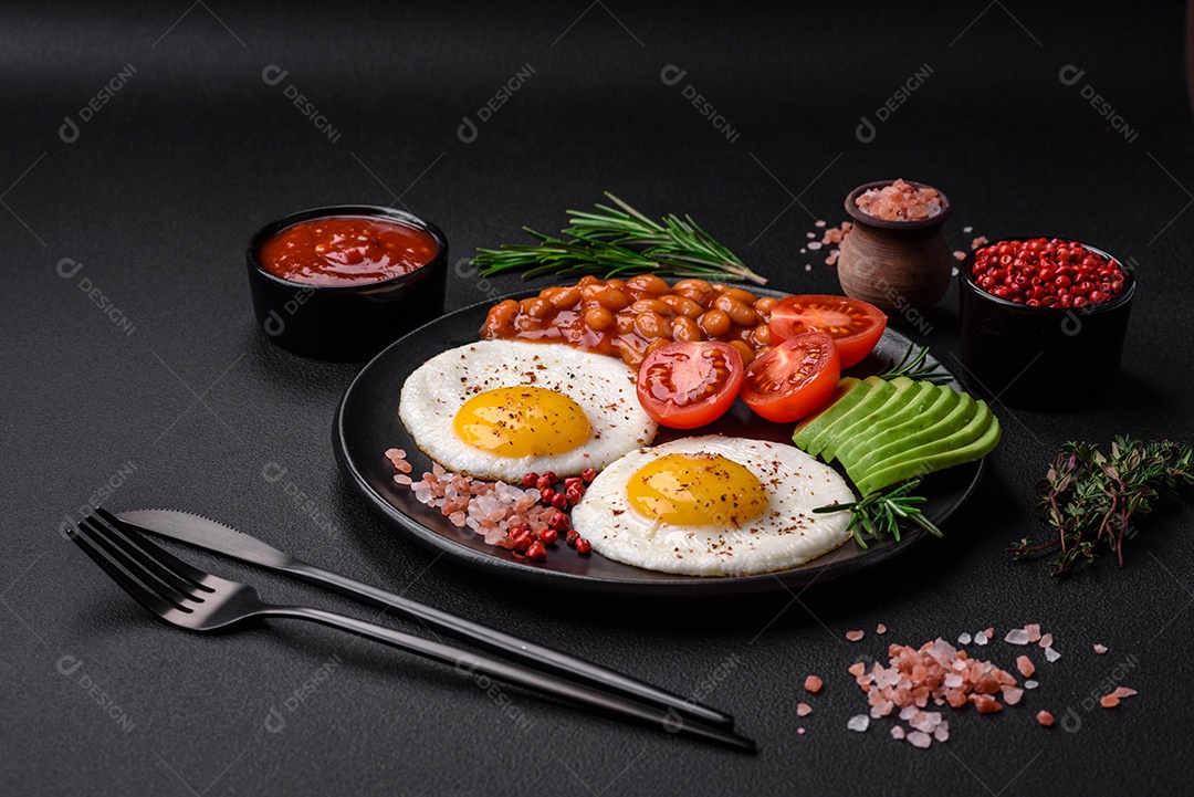 Delicioso café da manhã inglês nutritivo com ovos fritos, tomates, bacon e feijão em um fundo escuro de concreto