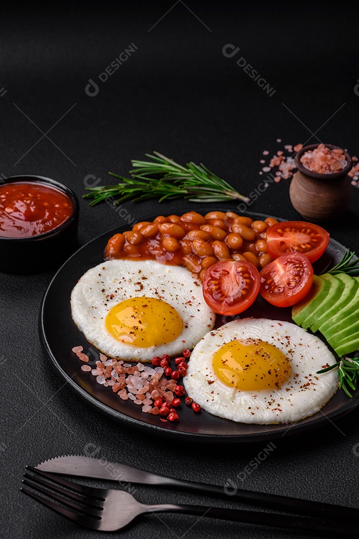 Delicioso café da manhã inglês nutritivo com ovos fritos, tomates, bacon e feijão em um fundo escuro de concreto