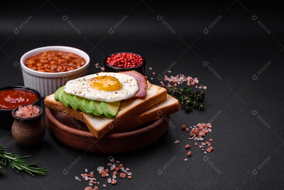 Delicioso café da manhã inglês nutritivo com ovos fritos, tomates, bacon e feijão em um fundo escuro de concreto