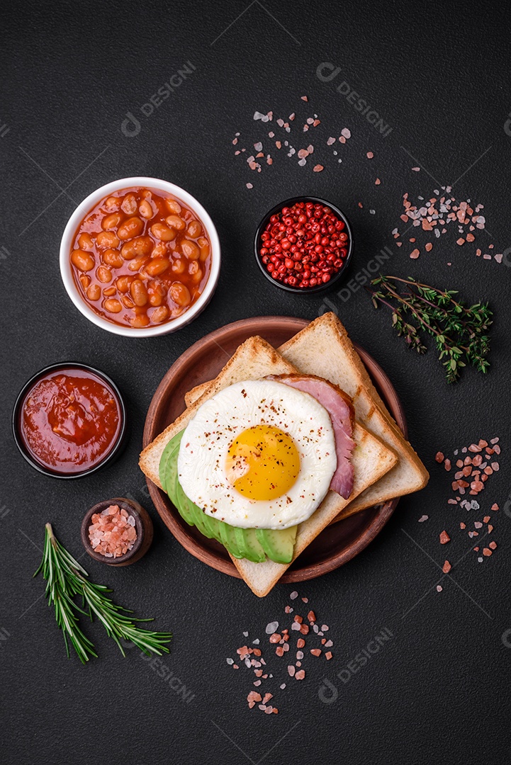 Delicioso café da manhã inglês nutritivo com ovos fritos, tomates, bacon e feijão em um fundo escuro de concreto