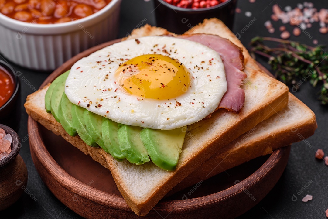 Delicioso café da manhã inglês nutritivo com ovos fritos, tomates, bacon e feijão em um fundo escuro de concreto