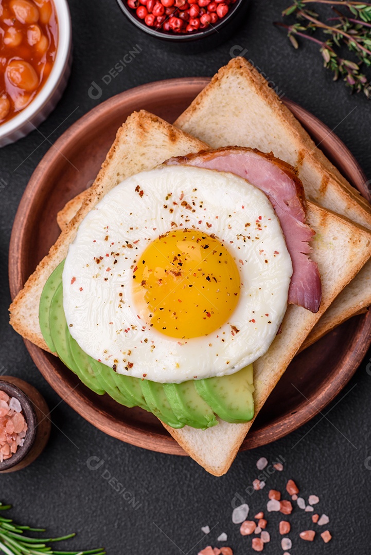 Delicioso café da manhã inglês nutritivo com ovos fritos, tomates, bacon e feijão em um fundo escuro de concreto