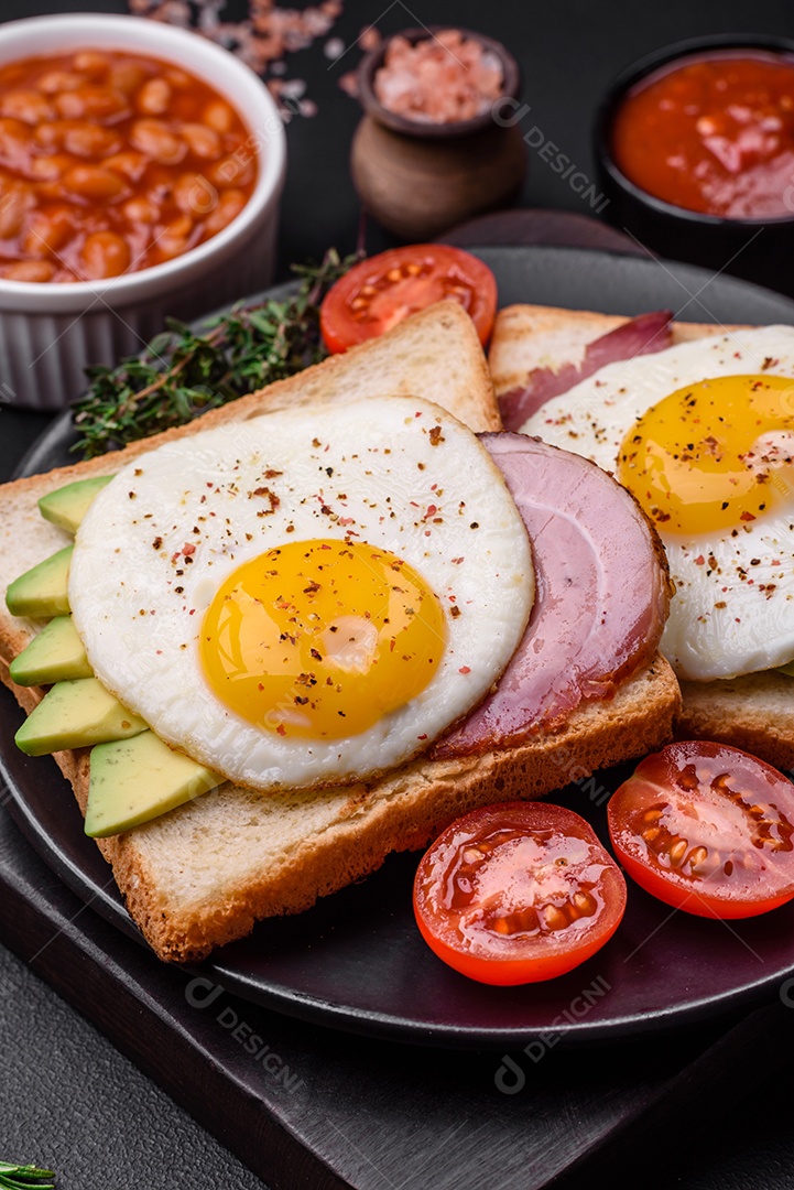 Delicioso café da manhã inglês nutritivo com ovos fritos, tomates, bacon e feijão em um fundo escuro de concreto