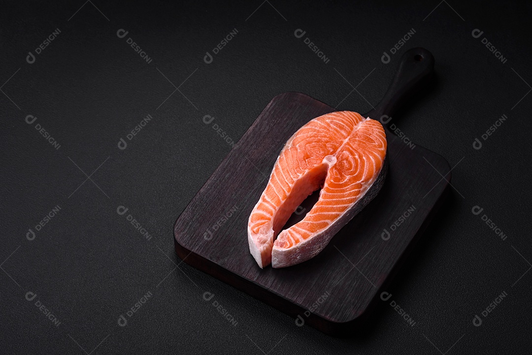 Bife de peixe vermelho cru fresco com especiarias e ervas sobre um fundo escuro de concreto