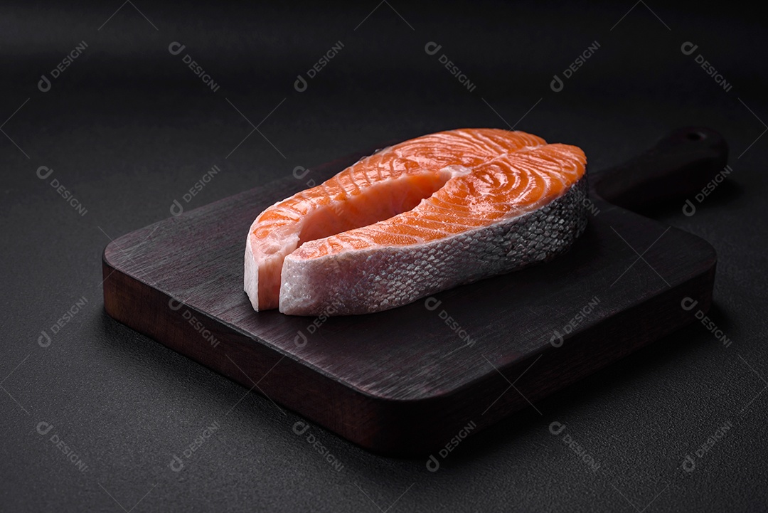 Bife de peixe vermelho cru fresco com especiarias e ervas sobre um fundo escuro de concreto