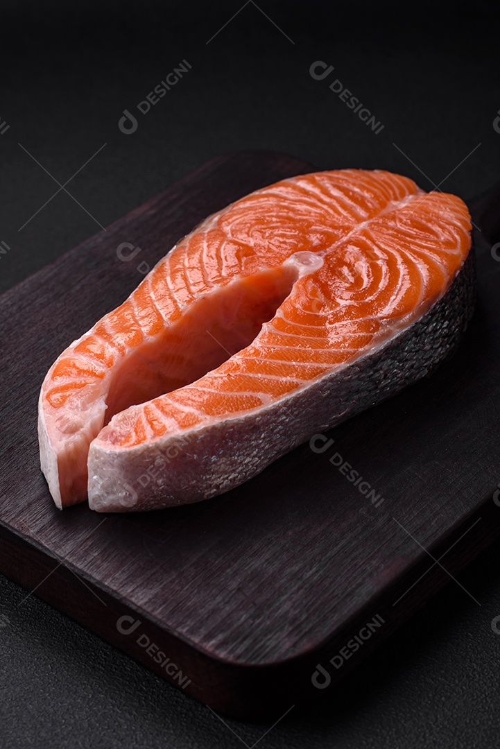 Bife de peixe vermelho cru fresco com especiarias e ervas sobre um fundo escuro de concreto