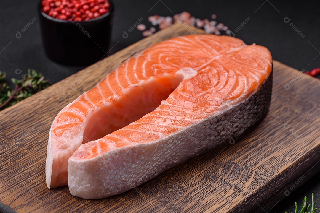 Bife de peixe vermelho cru fresco com especiarias e ervas sobre um fundo escuro de concreto