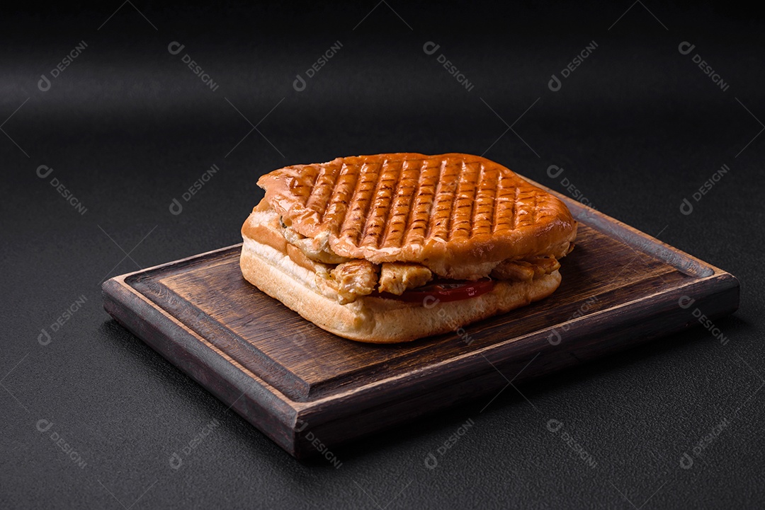 Delicioso sanduíche crocante com peito de frango, tomate, ketchup e especiarias em um fundo escuro de concreto