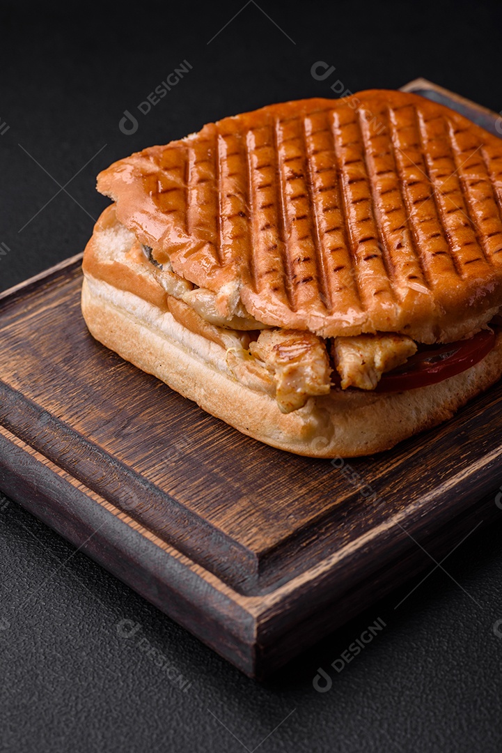 Delicioso sanduíche crocante com peito de frango, tomate, ketchup e especiarias em um fundo escuro de concreto