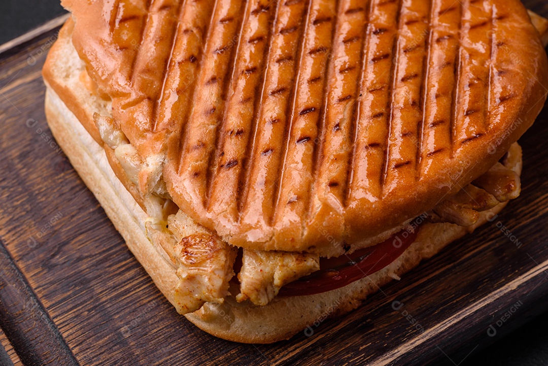 Delicioso sanduíche crocante com peito de frango, tomate, ketchup e especiarias em um fundo escuro de concreto
