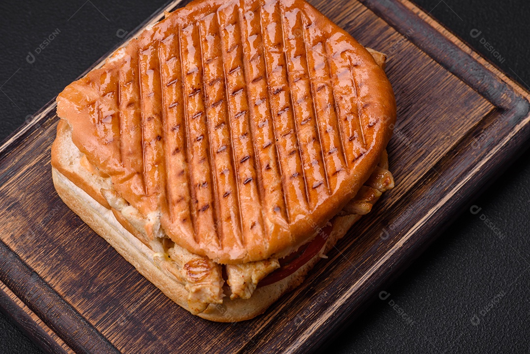 Delicioso sanduíche crocante com peito de frango, tomate, ketchup e especiarias em um fundo escuro de concreto