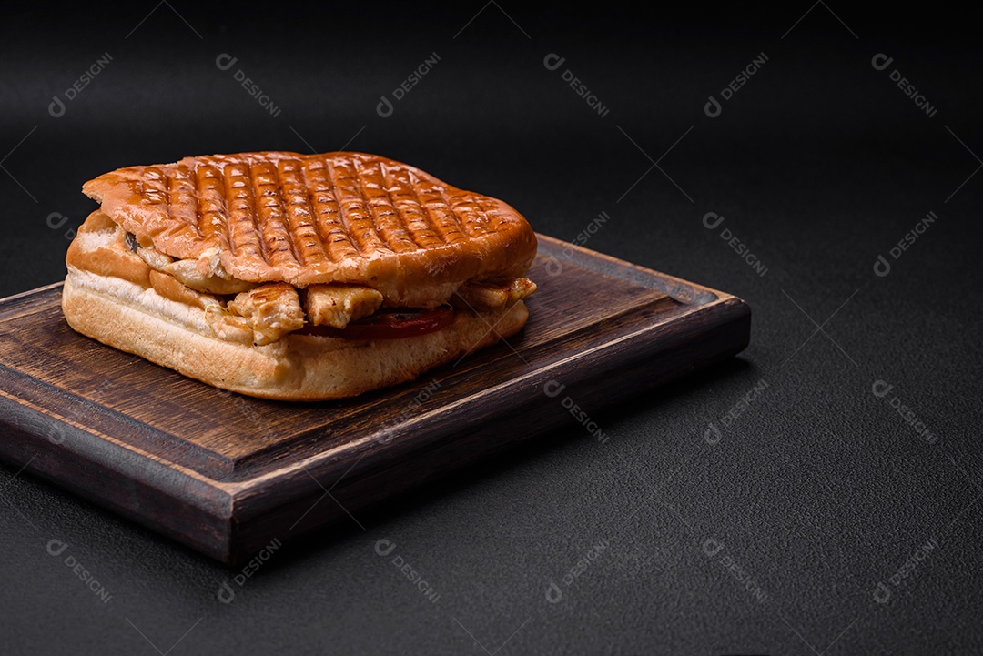 Delicioso sanduíche crocante com peito de frango, tomate, ketchup e especiarias em um fundo escuro de concreto