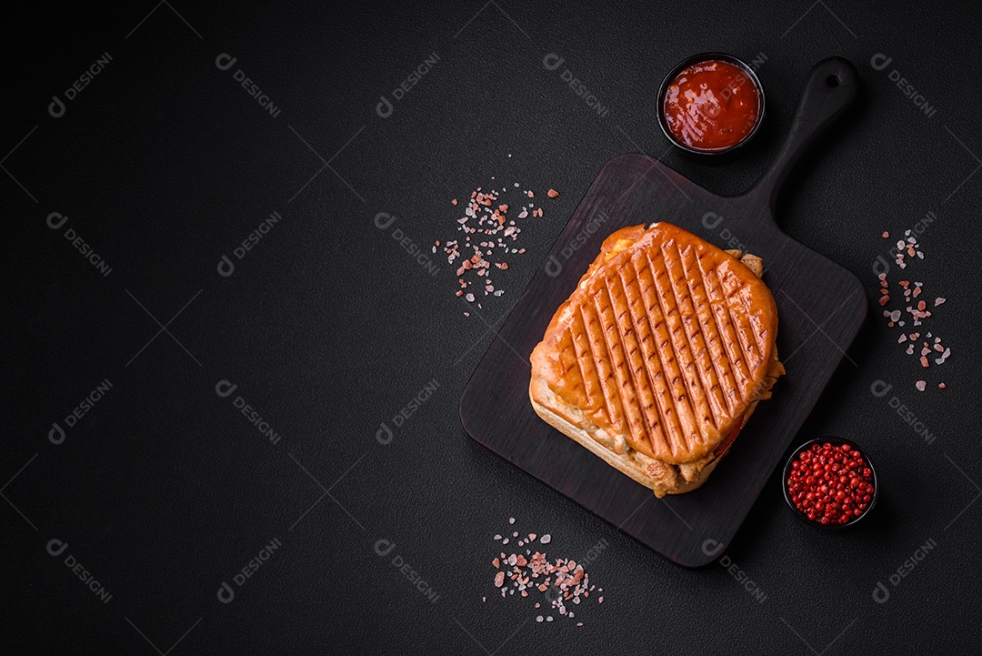 Delicioso sanduíche crocante com peito de frango, tomate, ketchup e especiarias em um fundo escuro de concreto