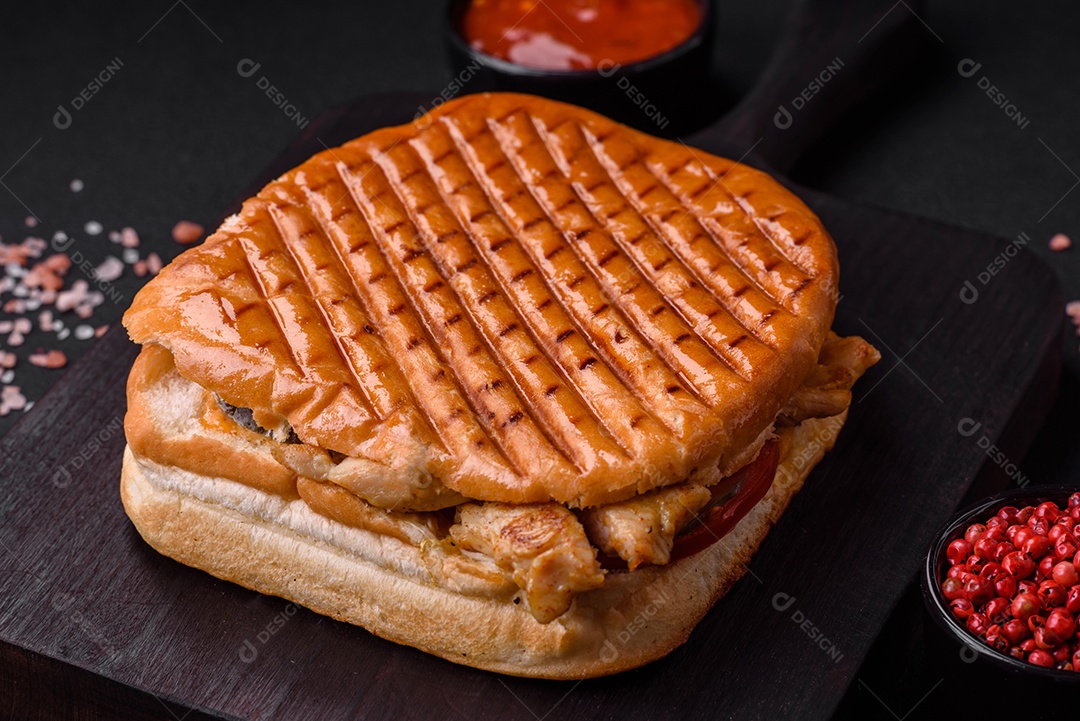 Delicioso sanduíche crocante com peito de frango, tomate, ketchup e especiarias em um fundo escuro de concreto
