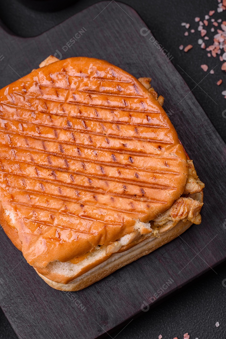 Delicioso sanduíche crocante com peito de frango, tomate, ketchup e especiarias em um fundo escuro de concreto