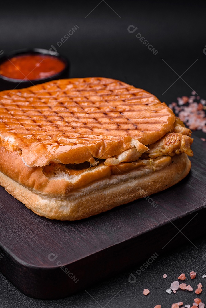 Delicioso sanduíche crocante com peito de frango, tomate, ketchup e especiarias em um fundo escuro de concreto