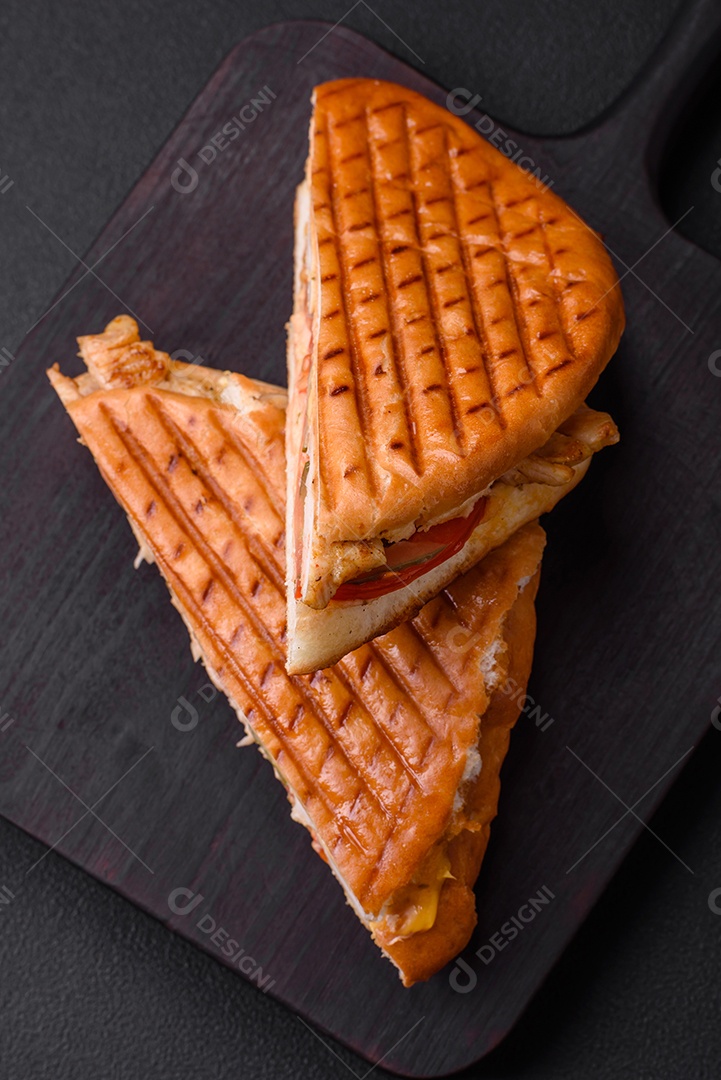 Delicioso sanduíche crocante com peito de frango, tomate, ketchup e especiarias em um fundo escuro de concreto