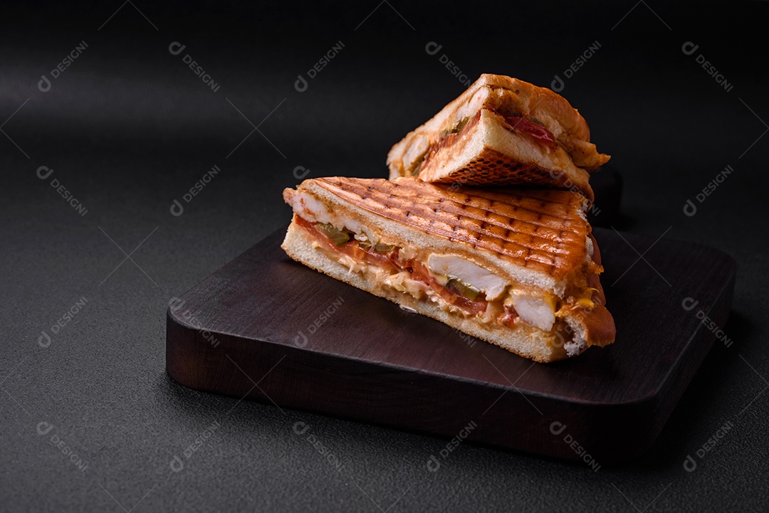 Delicioso sanduíche crocante com peito de frango, tomate, ketchup e especiarias em um fundo escuro de concreto