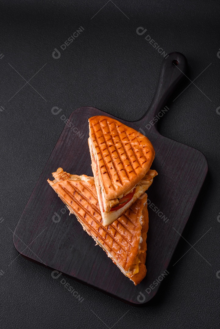 Delicioso sanduíche crocante com peito de frango, tomate, ketchup e especiarias em um fundo escuro de concreto