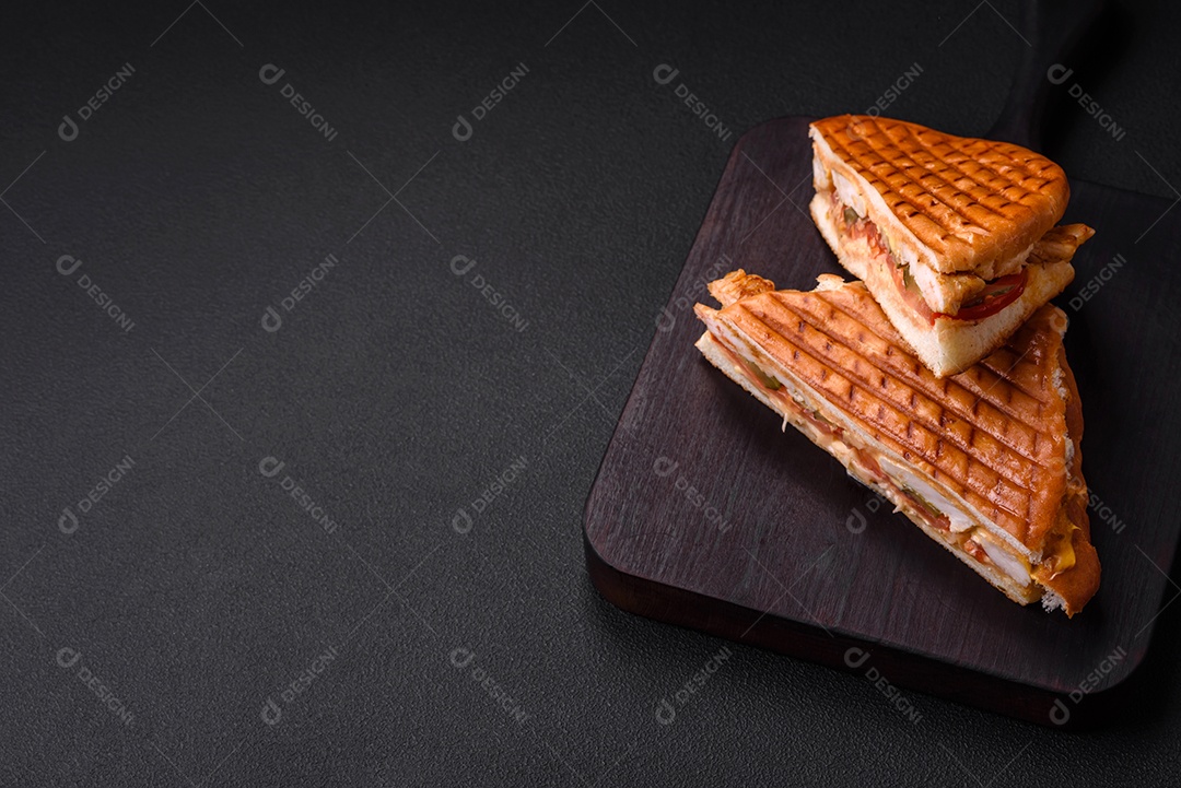 Delicioso sanduíche crocante com peito de frango, tomate, ketchup e especiarias em um fundo escuro de concreto
