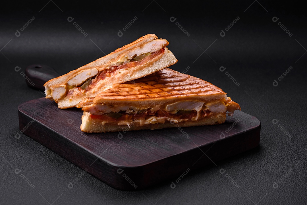 Delicioso sanduíche crocante com peito de frango, tomate, ketchup e especiarias em um fundo escuro de concreto