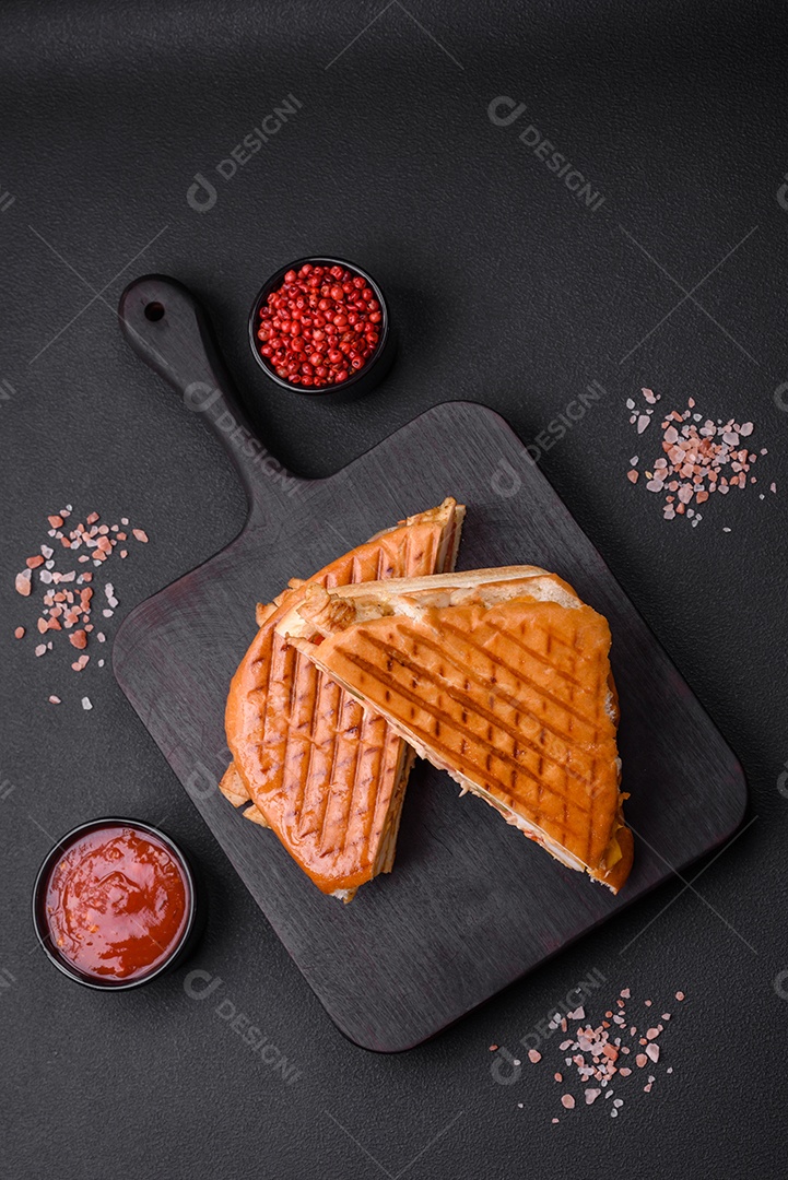 Delicioso sanduíche crocante com peito de frango, tomate, ketchup e especiarias em um fundo escuro de concreto