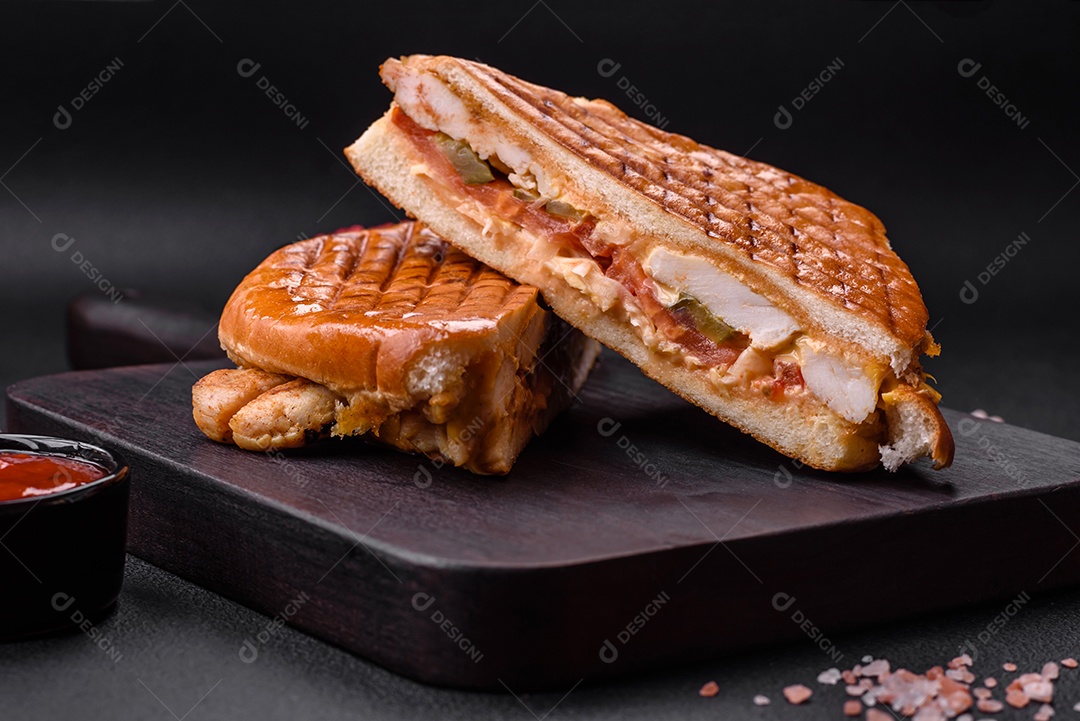 Delicioso sanduíche crocante com peito de frango, tomate, ketchup e especiarias em um fundo escuro de concreto