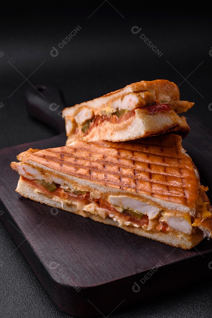 Delicioso sanduíche crocante com peito de frango, tomate, ketchup e especiarias em um fundo escuro de concreto