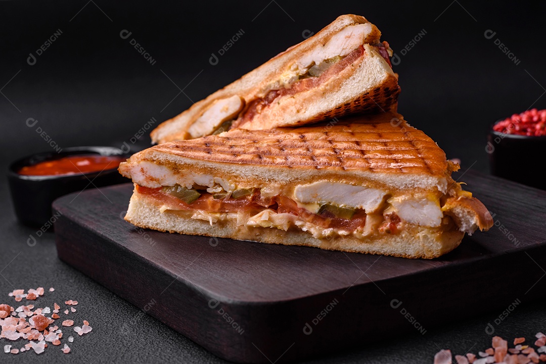 Delicioso sanduíche crocante com peito de frango, tomate, ketchup e especiarias em um fundo escuro de concreto